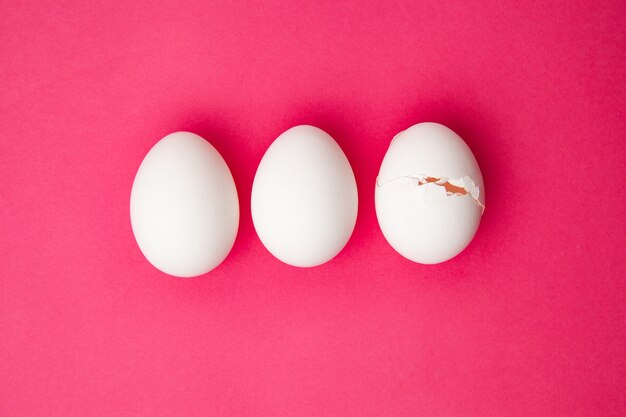 Set of whole and cracked eggs on pink surface