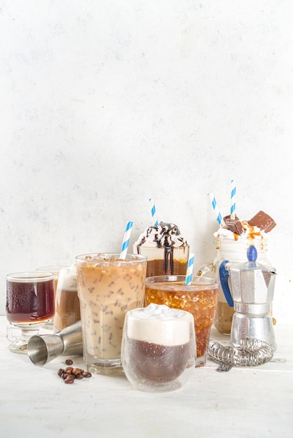 Set with different iced summer coffee drinks - espresso, frappe, latte, cappuccino, with whipped cream, syrup and crushed ice, in various glasses and  mugs on white background copy space