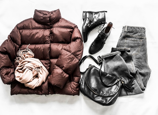 Set of women's autumn winter clothing down jacket black leather shoes gray jeans cashmere scarf bag on a light background top view