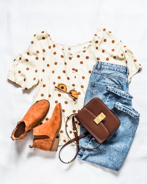 Set of women's summer clothes blue mom jeans polka dot blouse chelsea boots and cross body bag on a light background top view