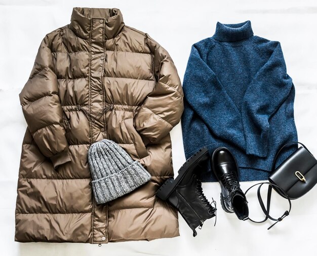 Set of women's winter clothes a warm down jacket sweater boots
with fur hat and leather bag on a light background top view fashion
season concept