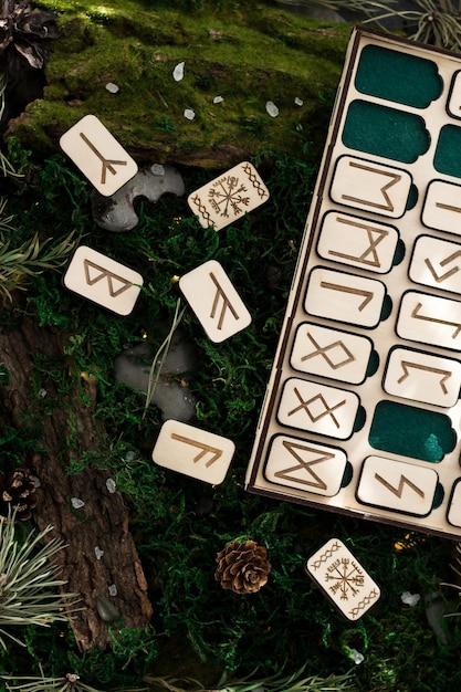 Set of wooden runes in a box lie on the moss in the forest. rectangular wooden platforms on which Scandinavian runes are carved lie on green moss surrounded by salt, cones, fir needles and bark