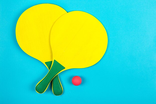 Set of yellow beach rackets on blue background with pink ball