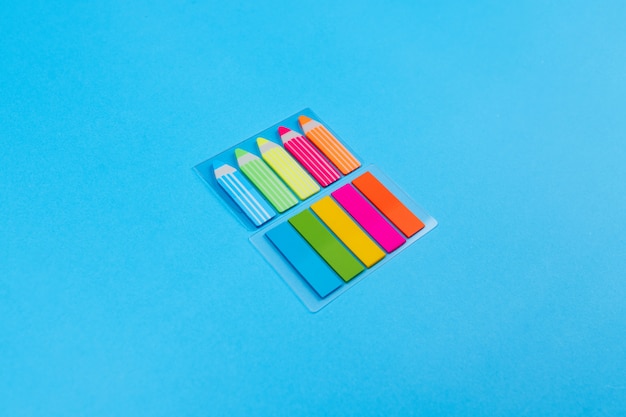 Sets of bright colored stickers in the form of stripes and pencils on transparent tablets located one above the other in the center on a blue . Place for advertising and recordings.