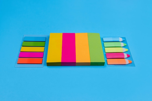 Photo sets of bright colored stickers in the form of stripes of yellow, pink, orange, green located on a blue  next to which are stickers in the form of stripes and pencils. place for advertising.