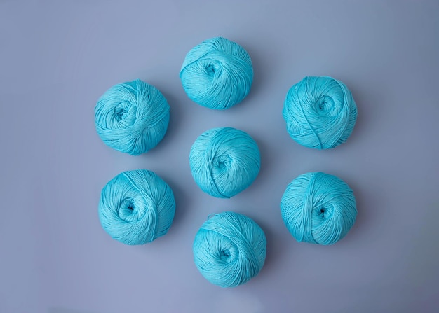 Seven balls of blue cotton yarn lie on a blue background