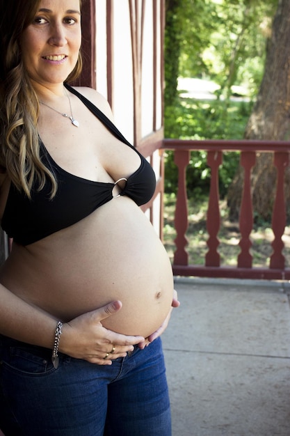 Photo seven months pregnant young woman dressed in black bikini and jeans