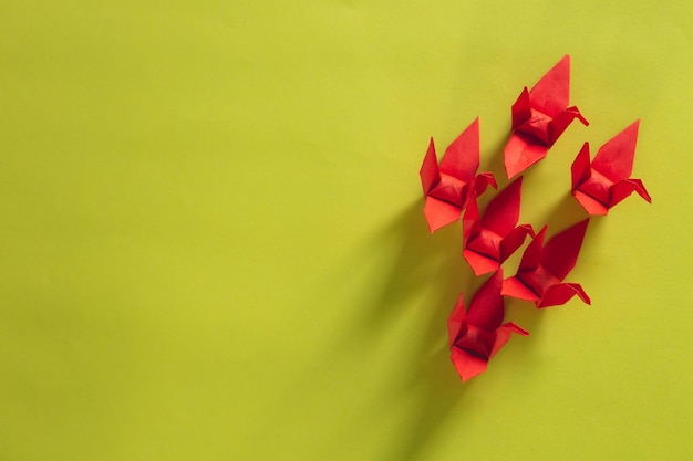 7개의 빨간 종이접기 새가 흰색으로 격리된 분홍색 새를 이끌고 날고 있습니다.빨간색 종이접기 종이학
