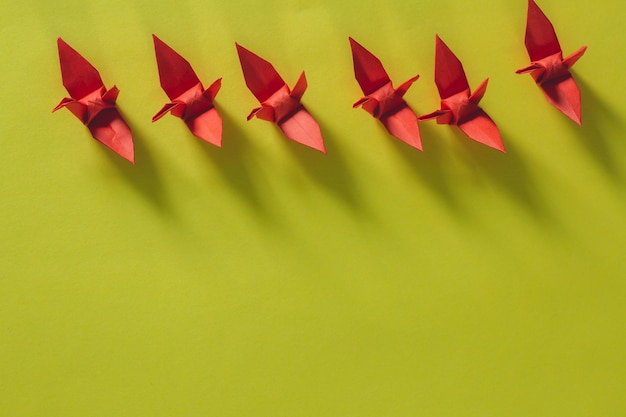 Seven red origami birds are flying leading by a pink bird\
isolated on whitered origami paper crane