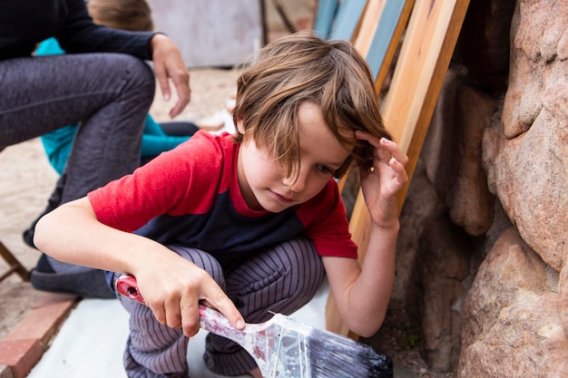 Seven year old boy using a paintbrush painting cardboard