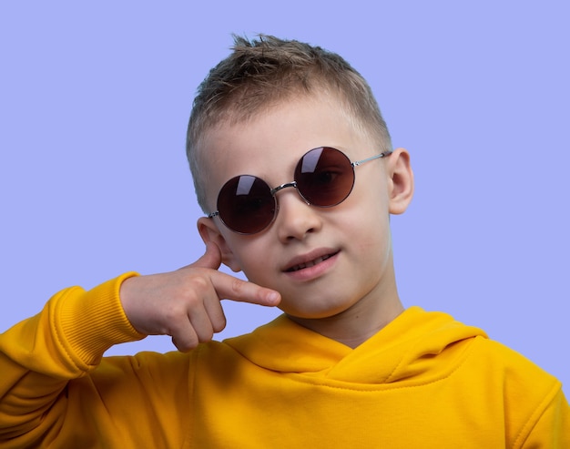 A seven-year-old boy in a yellow hoodie poses in front of a camera on a blue background