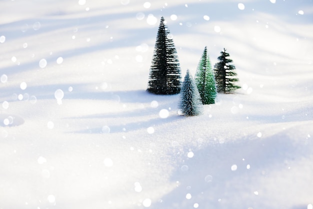 Several artificial small green synthetic fir trees standing on a sparkling frosty snow. Snow flakes falling in front of trees. Wallpaper