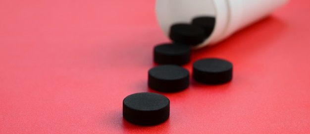 Several black tablets fall out of the plastic jar on the red surface