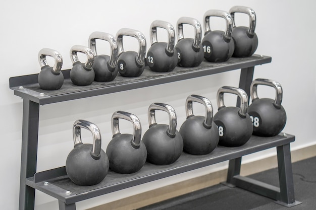 Several black weights different weights. Black metal weights kettlebell one row. Sports kettlebells in sport club. Weight Training Equipment