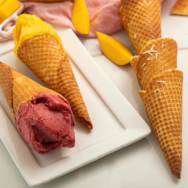Several cones of ice cream are on a white plate and one has a pink flower on it.