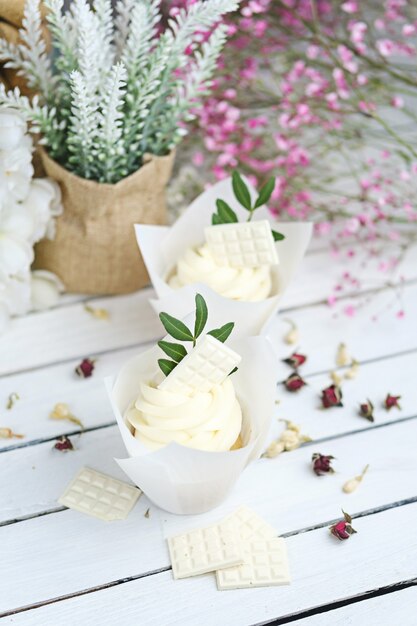 Several cupcakes and muffins with white butter cream on a white wooden table. 