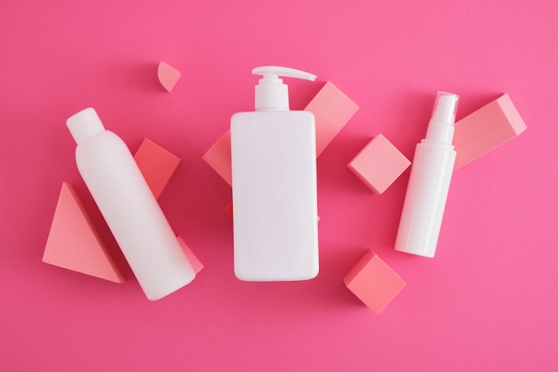 Several different white mock up cosmetics bottles on composition of geometric podiums, stands for product presentation on pink background. top view