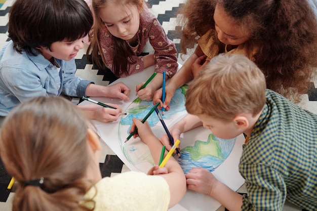 Foto diversi bambini diligenti disegnano il nostro pianeta con i pastelli