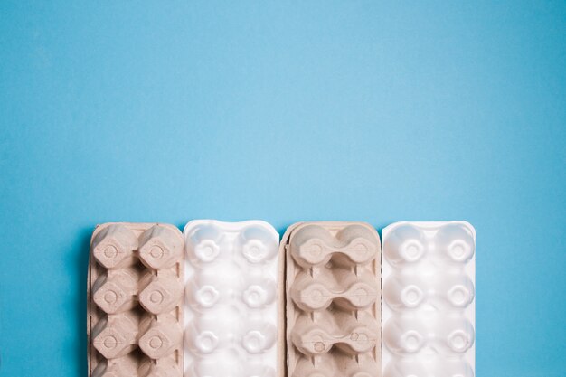 Several foam and cardboard packaging for eggs lie in a row on a blue surface