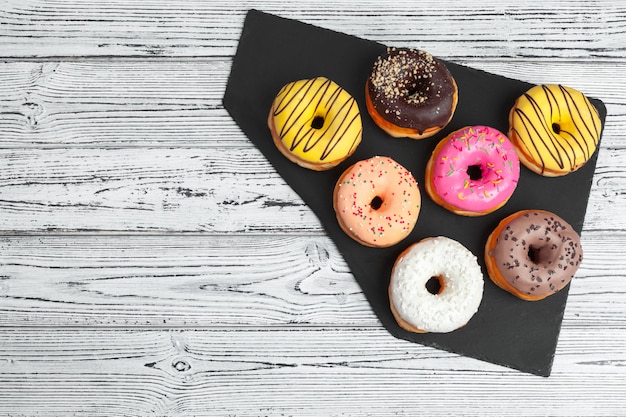 Several fresh donuts in a black ceramic plate on a wooden table