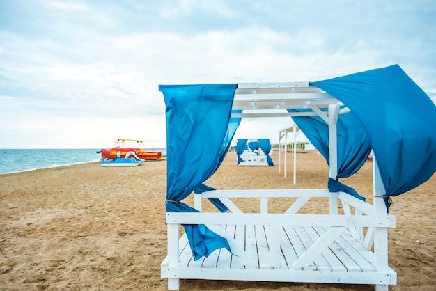 several gazebos on the beach at sunset with folding blue curtains no people