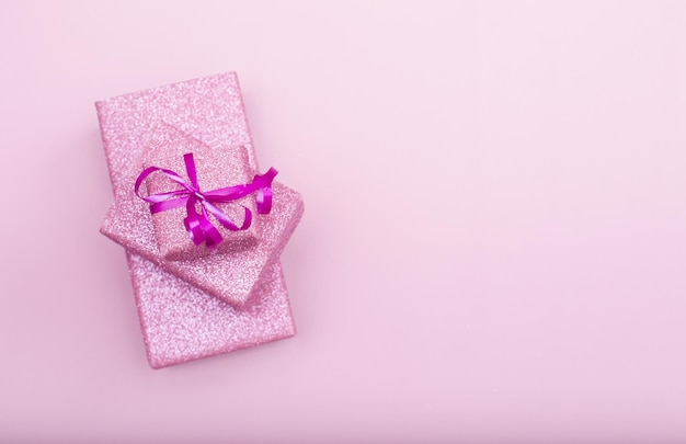 Several gift boxes lie on top of each other on a pink background with copy space