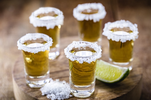 Several glasses of Mexican Gold Tequila with lemon and salt on wooden table