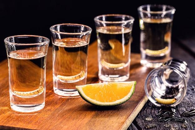 Several glasses of Mezcal (or mescal) is an exotic alcoholic drink from Mexico, distilled, variation of tequila, consumed with orange, and with a larva inside