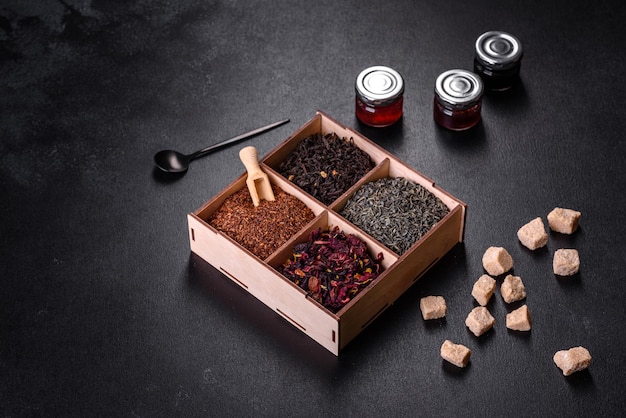 Several kinds of dry black tea with bergamot rooibos green and frame in a wooden box on a black concrete background