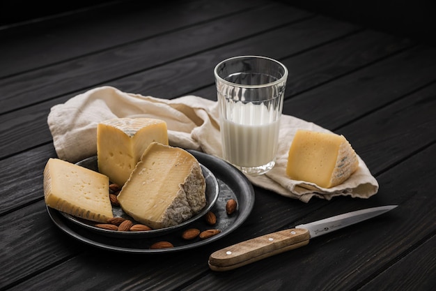 Several kinds of farm cheese and some almond on a steel tray, a napkin, a knife and a glass of milk, wooden table