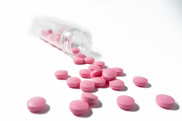 Several large bright pink tablets poured from a glass jar on white background