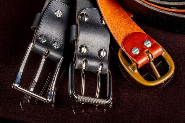 Photo several leather belts with a metal buckle on a dark background
