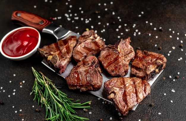 Photo several mini grilled beef t-bone steaks on the knife on stone table