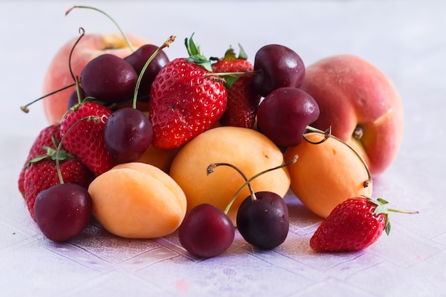 Several peaches, apricots, cherries and strawberries on a white tablecloth