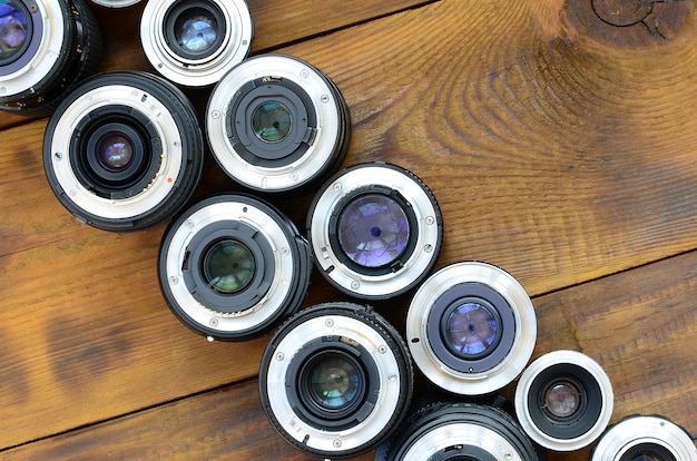 Several photographic lenses lie on a brown wooden background. Space for text