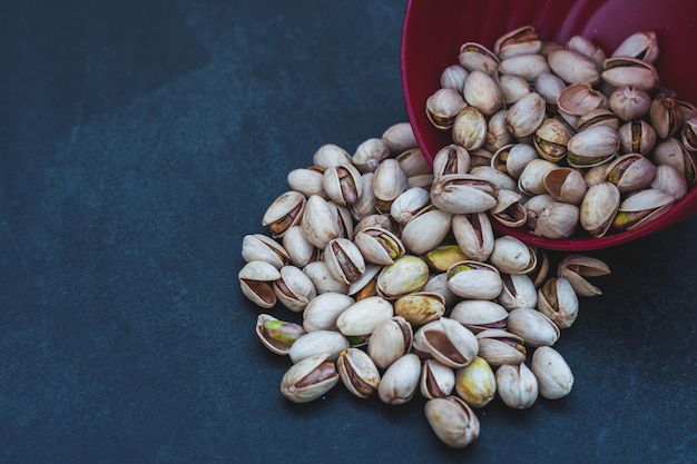 Several pistachios inside a red bowl with a black background