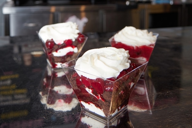 Several plates of chocolate dessert, cream and cherry berries, in the kitchen in a restaurant on a metal table, blurred surface