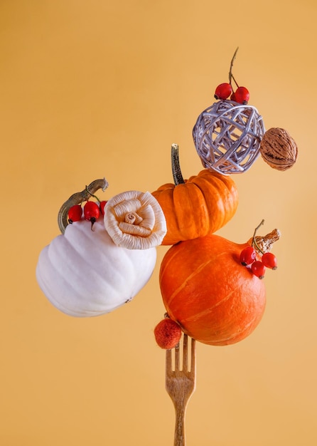 Several pumpkins, acorns and autumn leaves balancing on a wooden fork on a yellow background