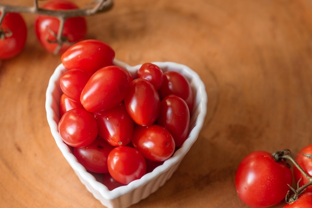 Several small tomatoes inside a white bowl on a wooden table