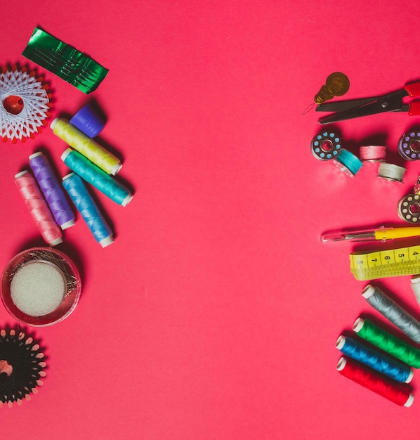 Several spools with colorful threads and metal bobbins sewing tools top view on bright pink background with copy space