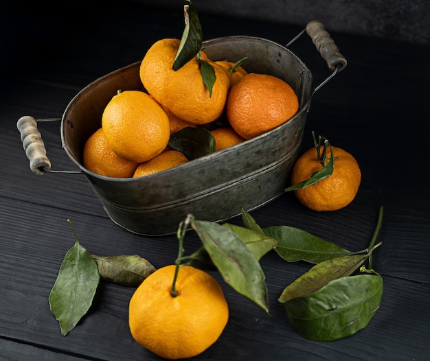 Several tangerines with leaves in a container lie on a black table