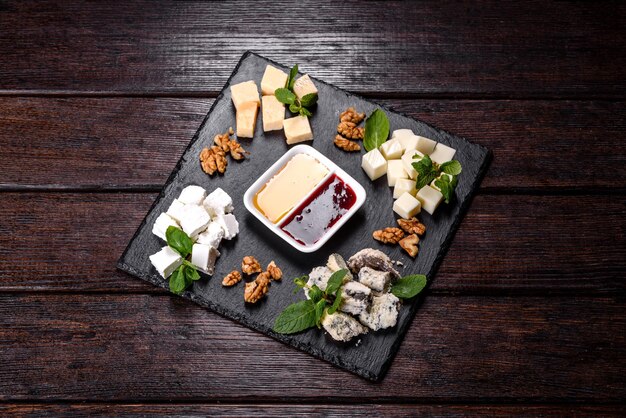 Several types of cheese on a shale tray with mint and sweet sauces
