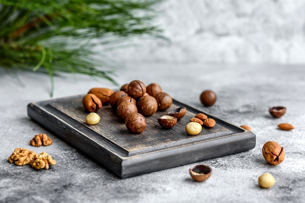 Photo several types of nuts with of spruce branches on a wooden cutting board on concrete