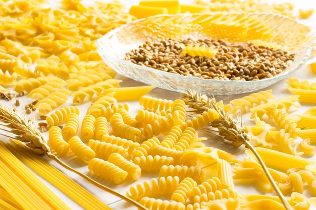 Several types of pasta, spikelets of wheat, wheat grain on white