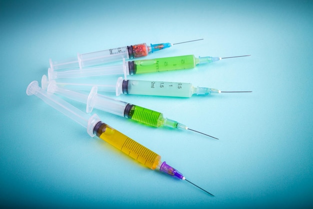 Several various syringes with multicolored medicine on blue background drugs or vaccine injections