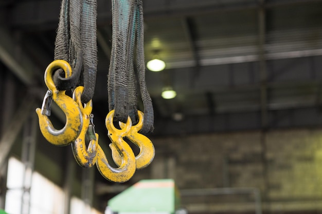 Several yellow cargo hooks hanging on dirty oiled textile slings