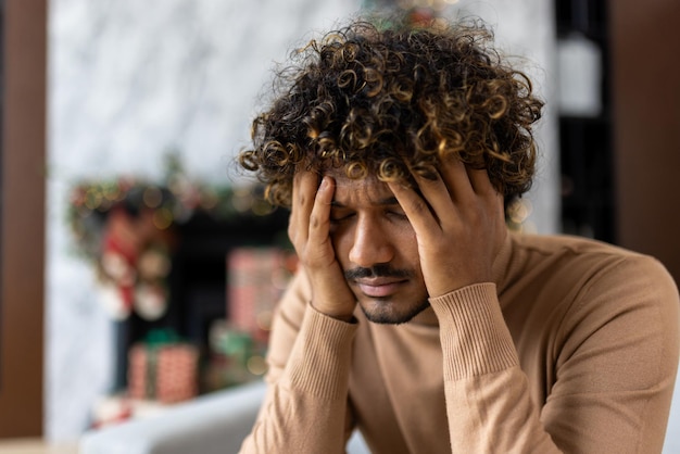 Severe hangover headache and migraines man holding head sitting on sofa in living room for christmas