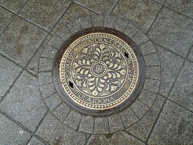 Sewer metal heavy hatch with ornament old historic street in\
the city center of budapest hungary engineering urban systems\
lettering and forged patterns