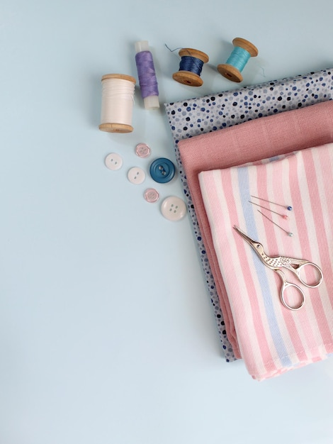 Photo sewing accessories and fabric on a blue background sewing threads needles pins fabric buttons and sewing centimeter top view flatlay