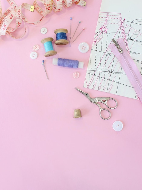 Photo sewing accessories and fabric on a pink background sewing threads needles pins fabric buttons and sewing centimeter top view flatlay